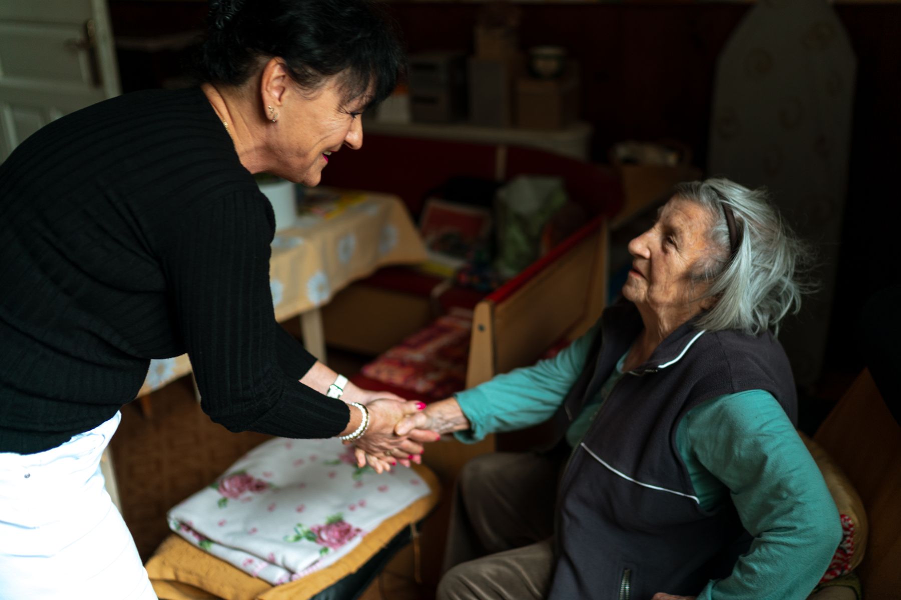 A caregiver leaning in to greet a resident and take her hands