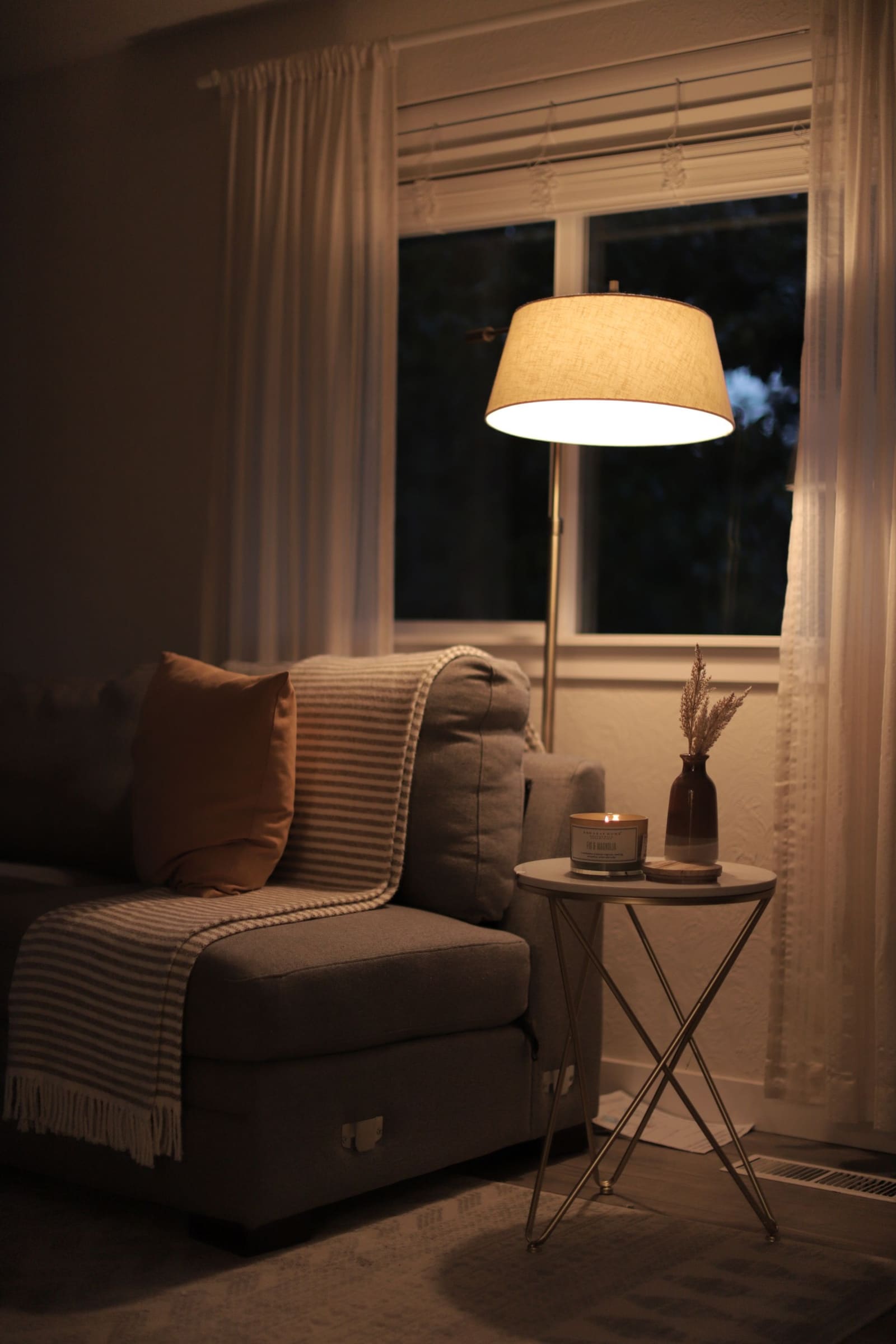 The living room at dusk with a warm lamp on and the hallway light glowing